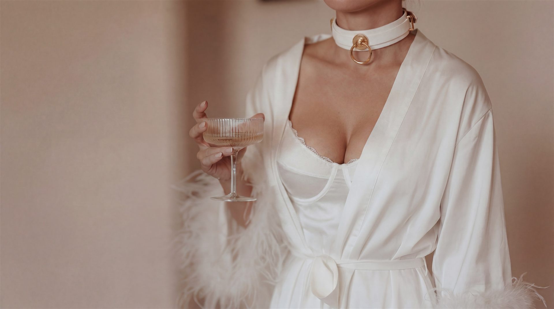 Bride in a feathered white robe holding a champagne coupe — an intimate bridal ritual